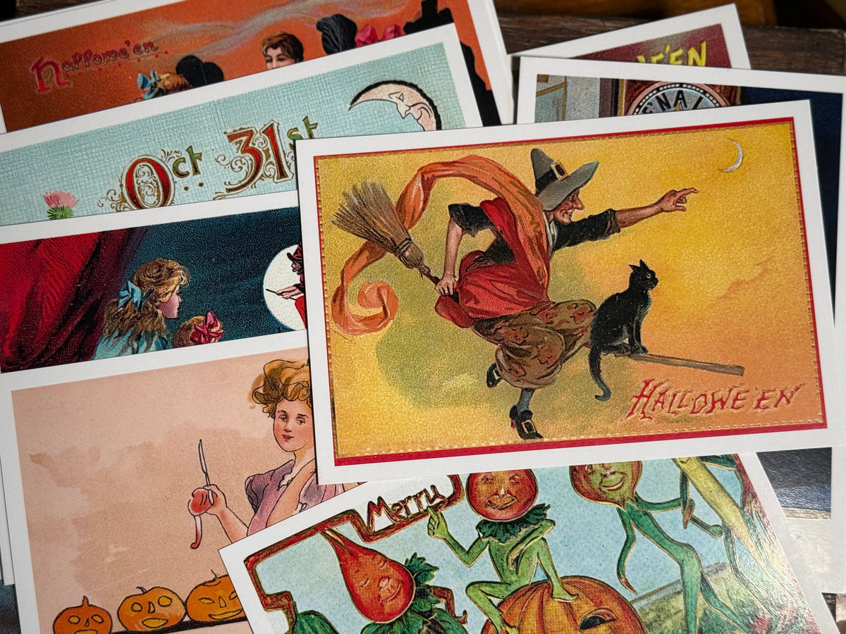 A collection of vintage-style Halloween cards fanned out on a dark wooden surface, featuring classic illustrations of witches, pumpkins, ghosts, and a cat.